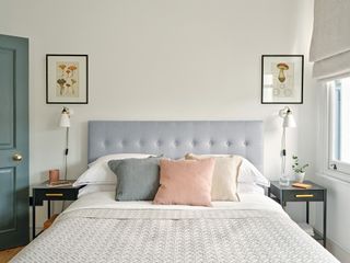 White bedroom with grey upholstered bed, light grey throw and grey and pink cushions, black bedside tables and mushroom prints