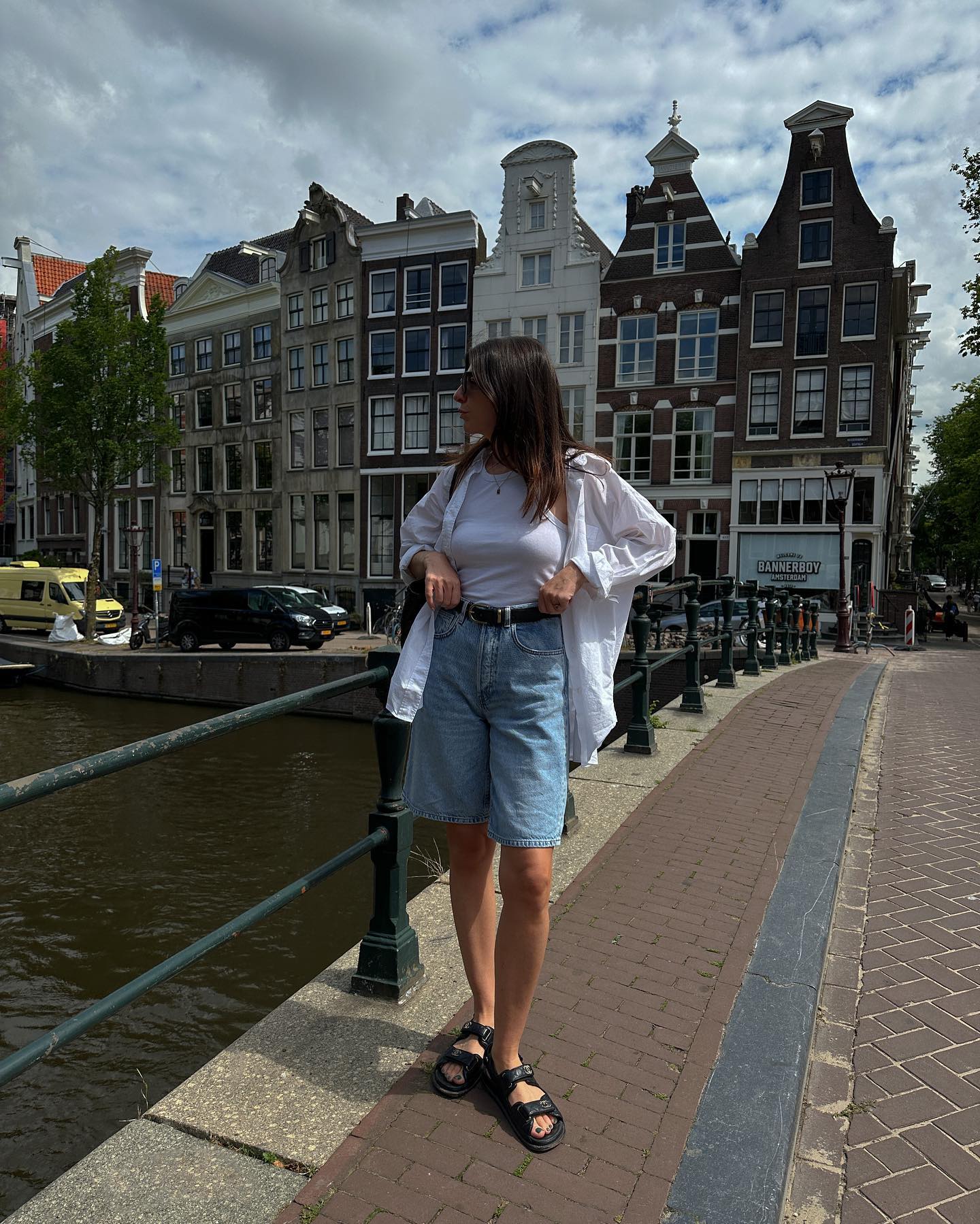 Woman on street wears long denim shorts, white shirt and sandals