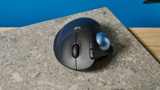 A black Logitech Ergo M575 ergonomic mouse with a teal trackball on the left side