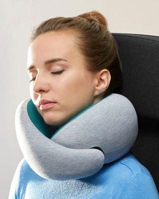 A woman wears the gray Ostrichpillow Go Neck Pillow