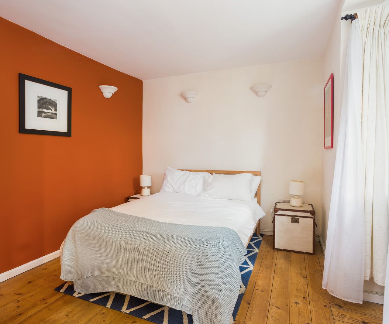 A bedroom with an orange wall and a wooden floor