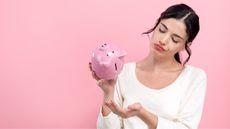 A woman looks sad that she's holding her piggy bank upside down and nothing's coming out.