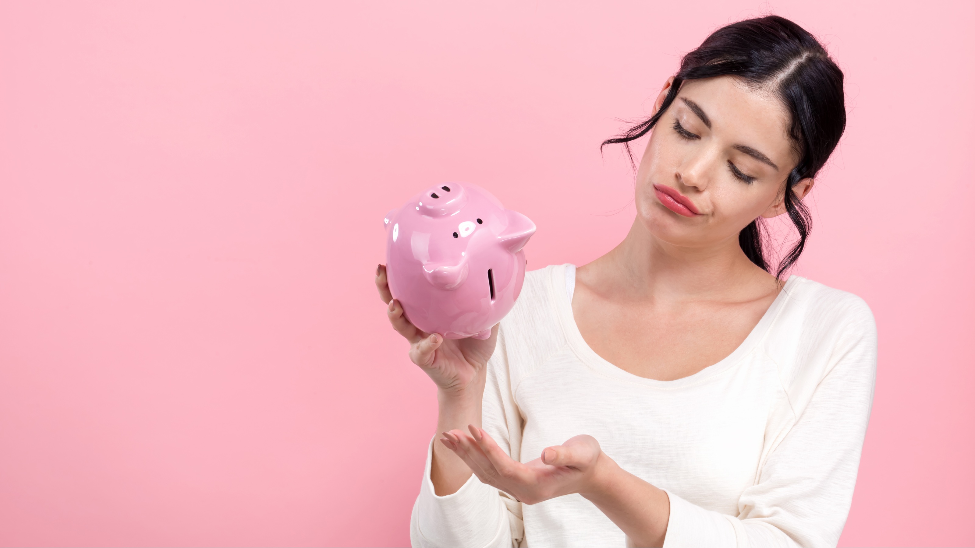 A woman looks sad that she's holding her piggy bank upside down and nothing's coming out.
