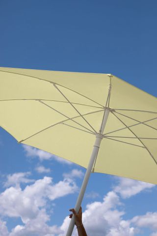 A hand holding a yellow parasol with the blue sky and clouds behind it.