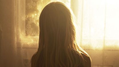 a person with long hair looking out a window