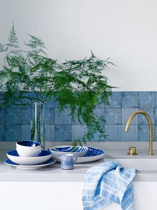 kitchen with white cabinetry and walls and blue tiled backsplash and tableware