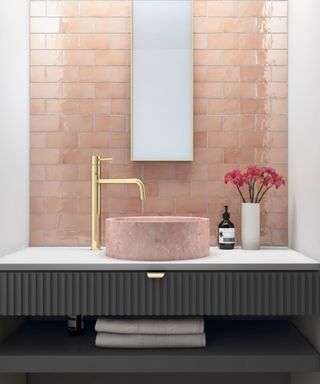A pink quartz zink bowl, gold taps and matching pink gloss tiles with a thin rectangular mirror