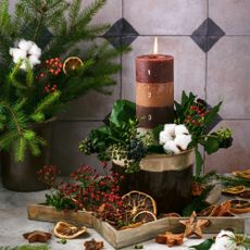 Burning Christmas layers candle with 4 Advent numbers decorated with natural material, slices of dried orange, fir, ivy and rose hip berries branches