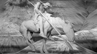 A black and white photograph of the Trail of Tears/End of the Trail statue. It depicts a Native American slumped on his horse whilst holding a spear (pointing downwards). The horse is also very weary looking.