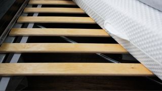 A close up of wooden bed frame slates with white mattress coming in top right corner.