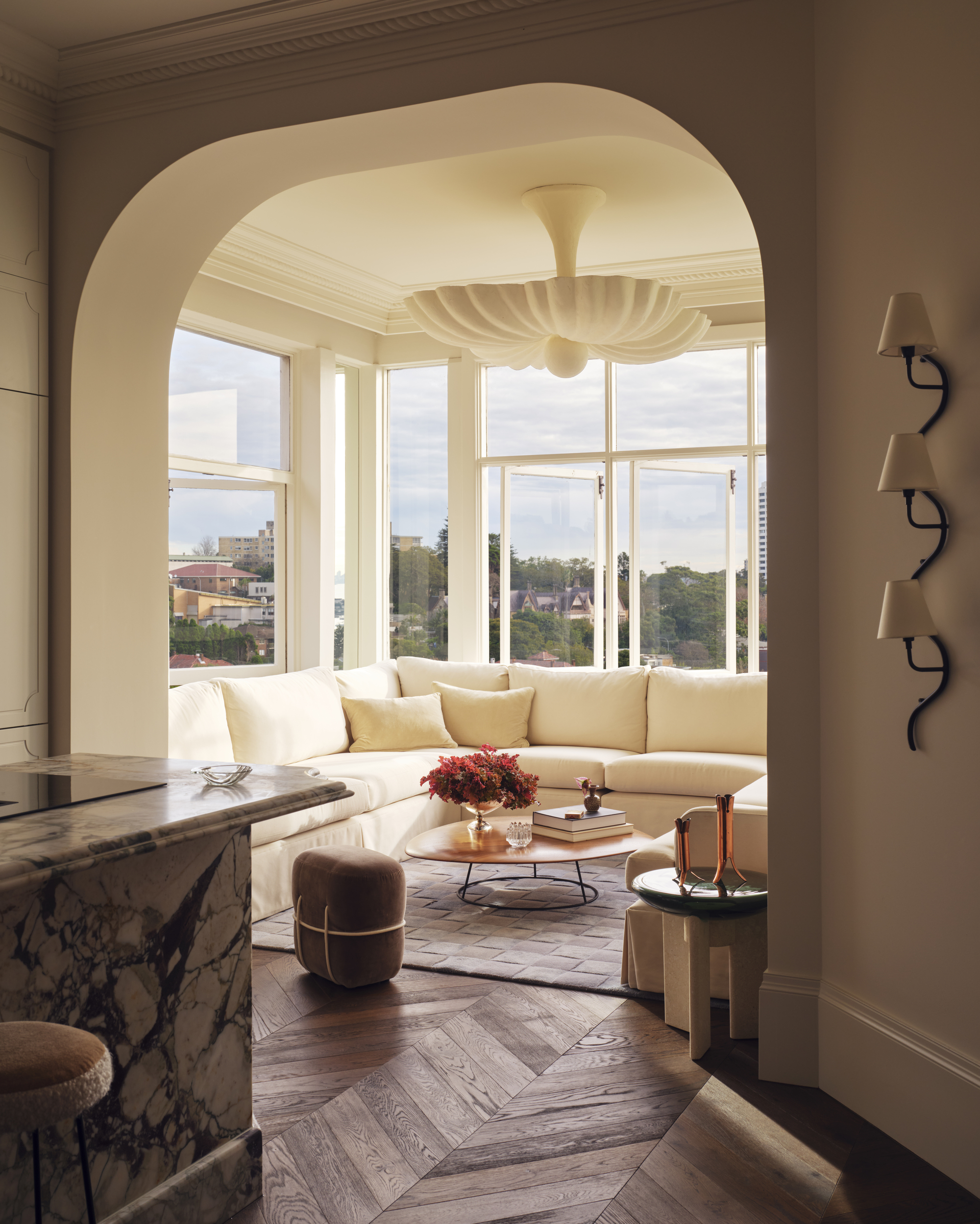 a small living room with an arched doorway, white sofa, herringbone flooring and sculptural pendant light