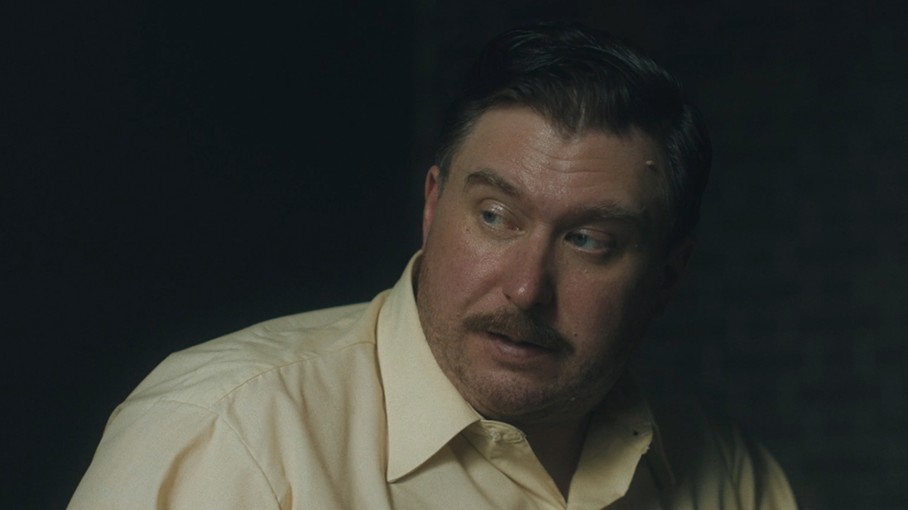 Michael Chernus with a mustache, looking to his right in Devil In Disguise