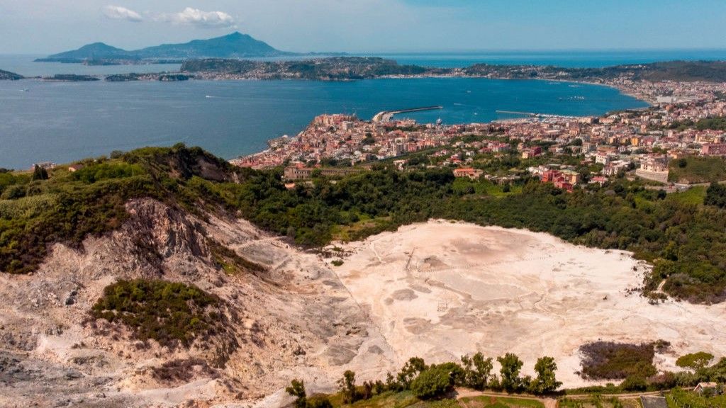 A view of the Solfatara crater of Italy&#039;s Campi Flegrei volcano caldera with the Mediterranean Sea in the background.