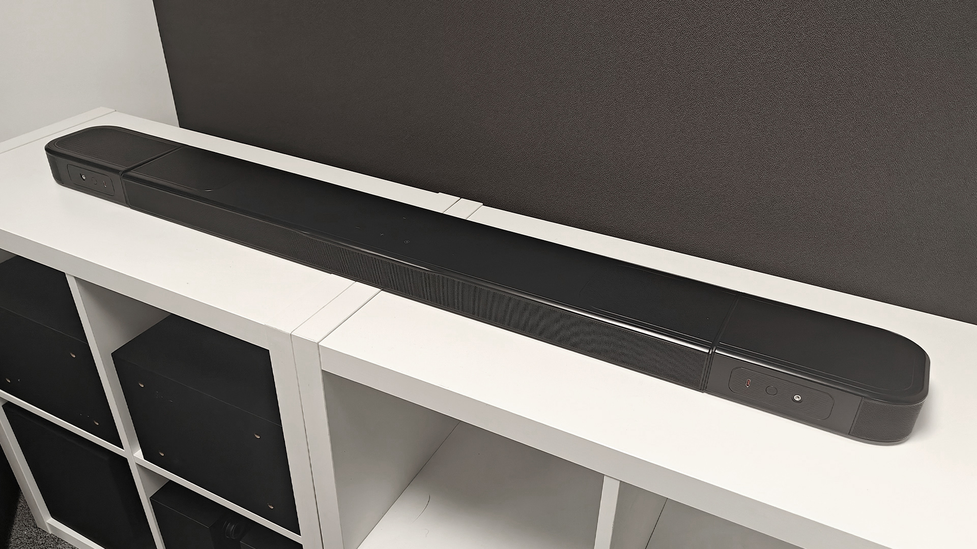 JBL Bar 1000MK2 soundbar system on white wooden shelving unit showing soundbar with surrounds attached