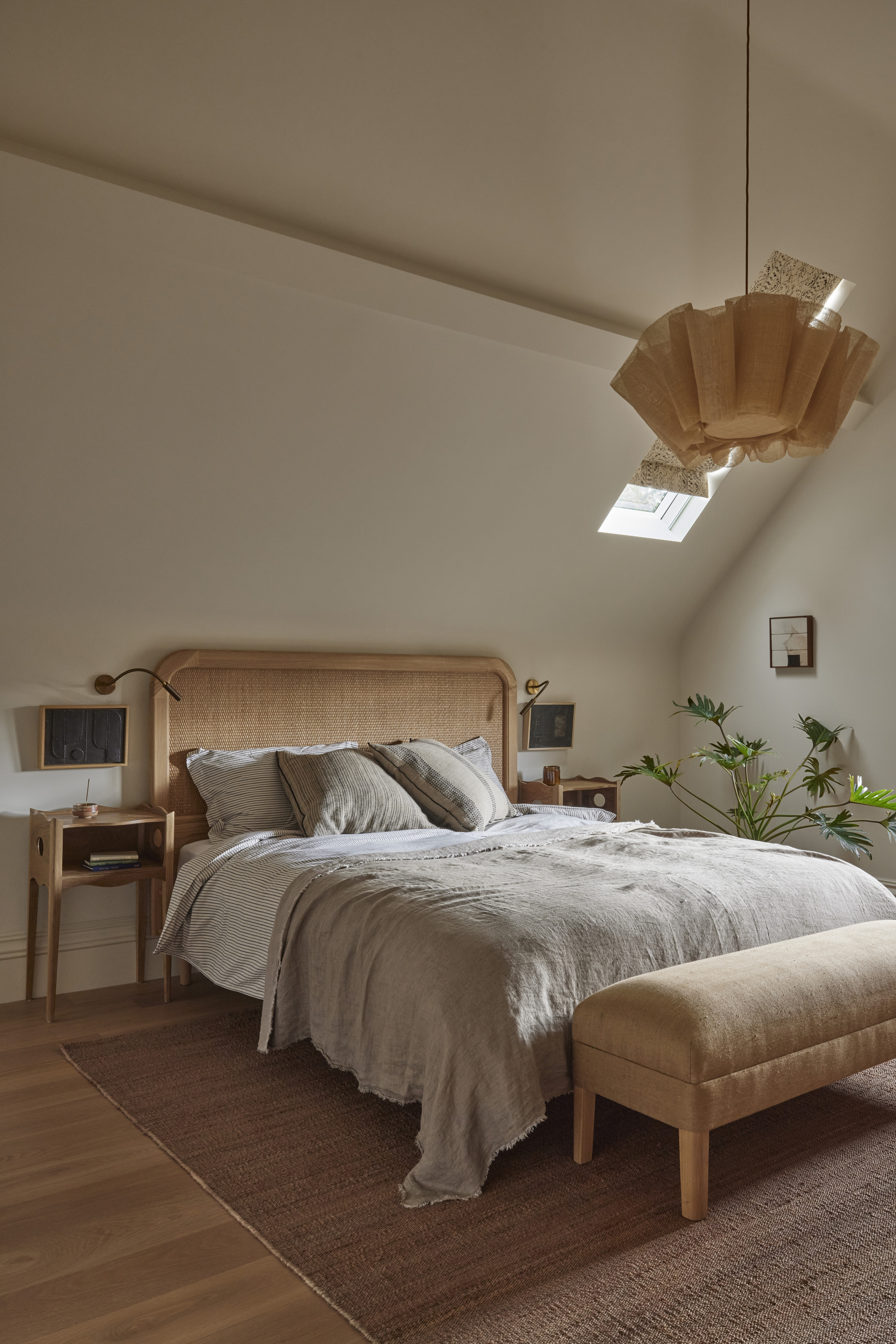 A neutral, Scandi style bedroom with a rattan headboard, a woven lamp shade, and linen bedding