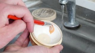 A brush being washed with brush soap over a sink