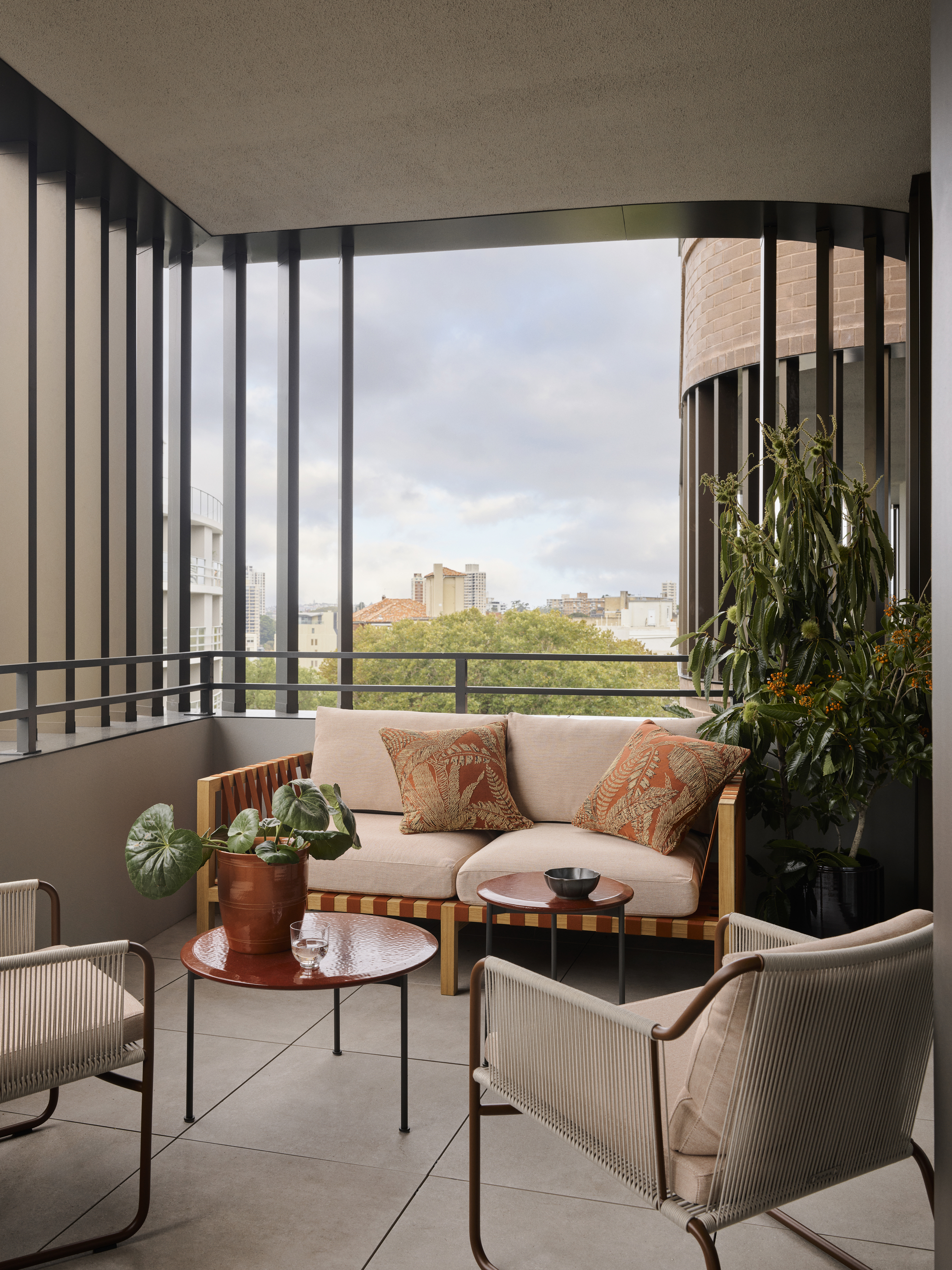 balcony with sofa with cushions and two armchairs and round coffee table with pot plant