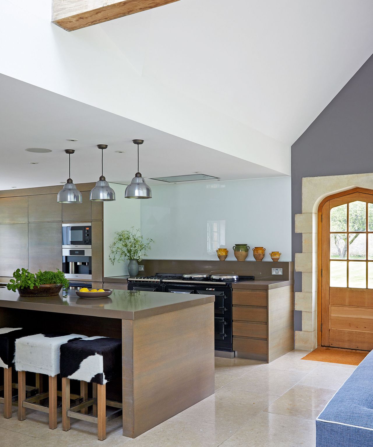 Neutral kitchen with wood cabinets, cowhide stools and metal pendant lights