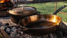 A cast iron Dutch oven and skillet on an outdoor charcoal pit.