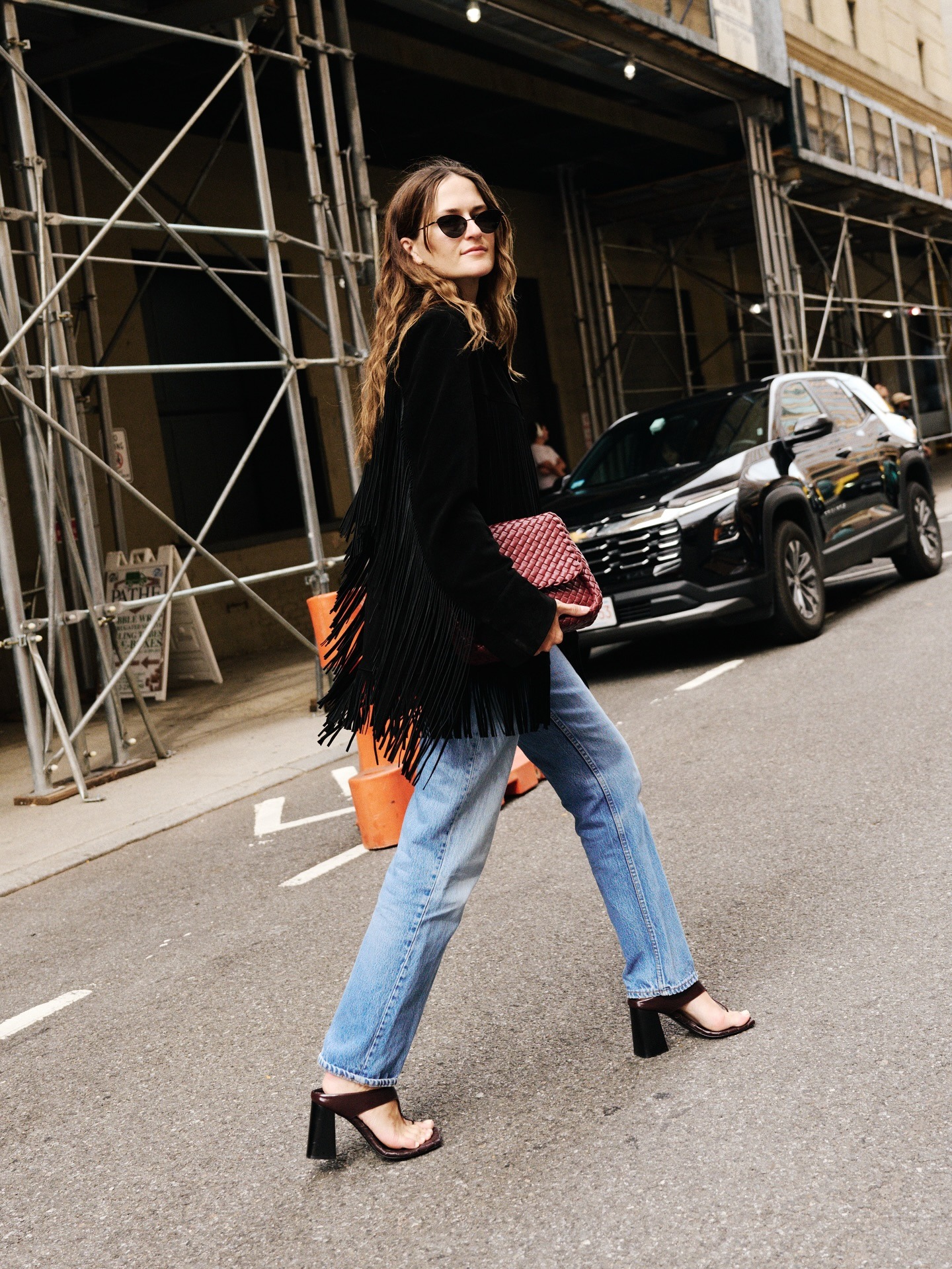 A photo of Eliza Huber wearing a black fringe jacket with jeans and heeled sandals.