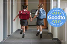 Two young girls running through a school corridor with rucksacks on