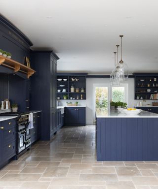 A kitchen with dark blue cabinets, a glass door, a kitchen island, and light gray stone flooring