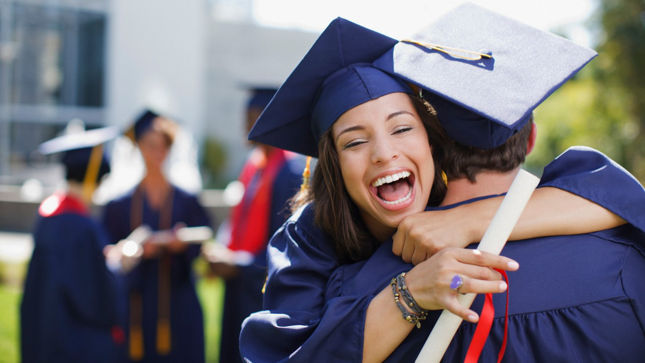 A woman in a cap and gown hugs another graduate