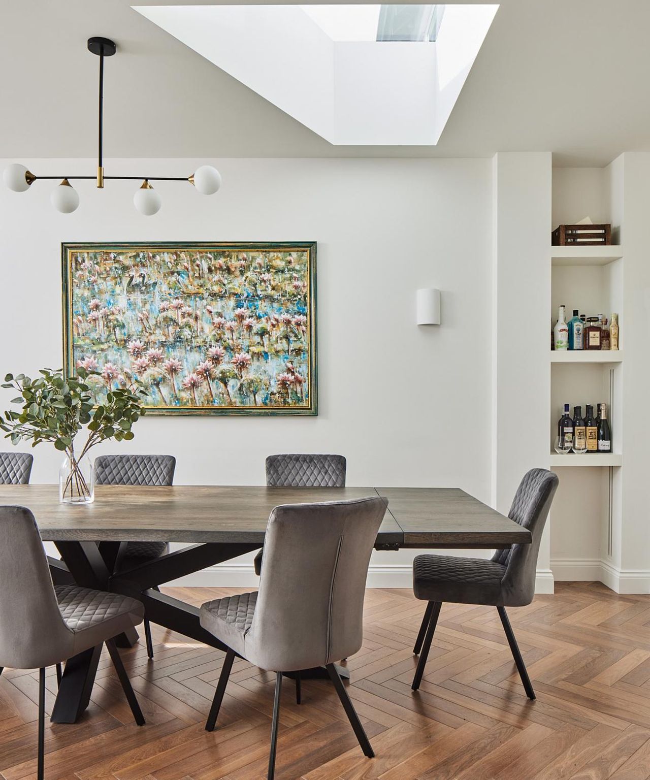 inside of living room extension showing media wall with blue units and shelves, wooden floor, skylight above dining table and white built in shelving