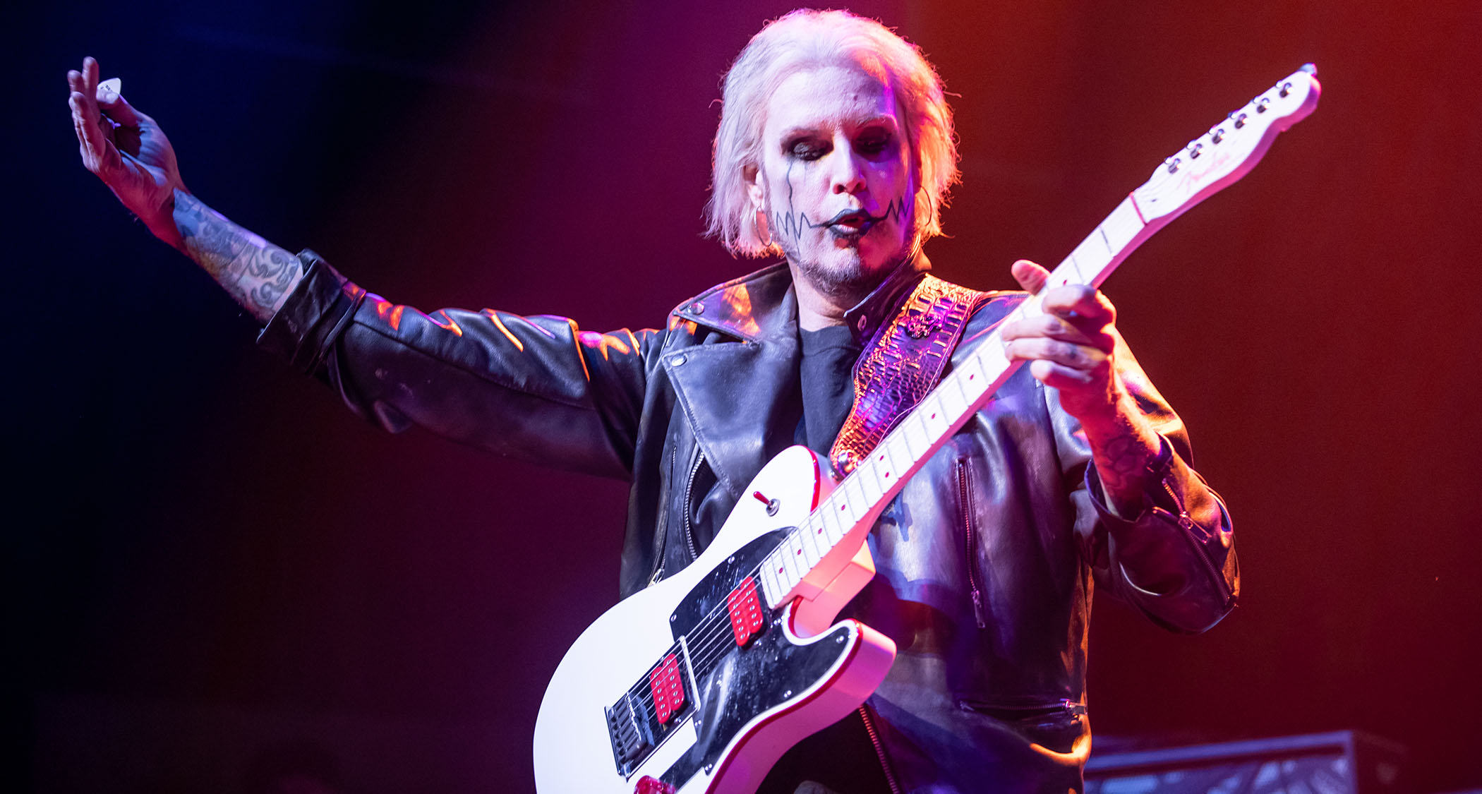 John 5 wears a black biker jacket and holds his picking in the air as he performs with his signature &quot;Ghost&quot; Telecaster