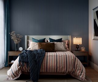 bedroom with denim blue wall panelling behind bed with pale blue headboard, striped bedding and two bedside tables in dark wood