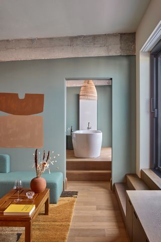 Suite with pale blue walls in living room, leading through to freestanding bath up steps