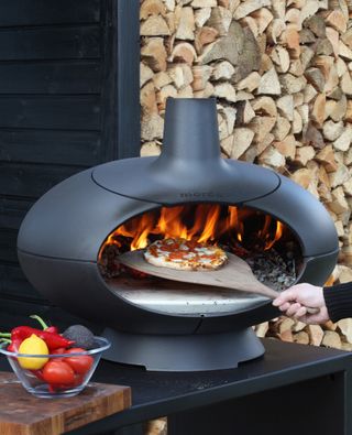 person sliding a pizza into a pizza oven to cook it