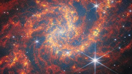 A red and orange spiral galaxy image with lots of stars.