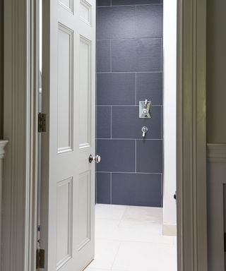 A dark blue tiled wall and white tiled floor illustrating small wet room ideas.