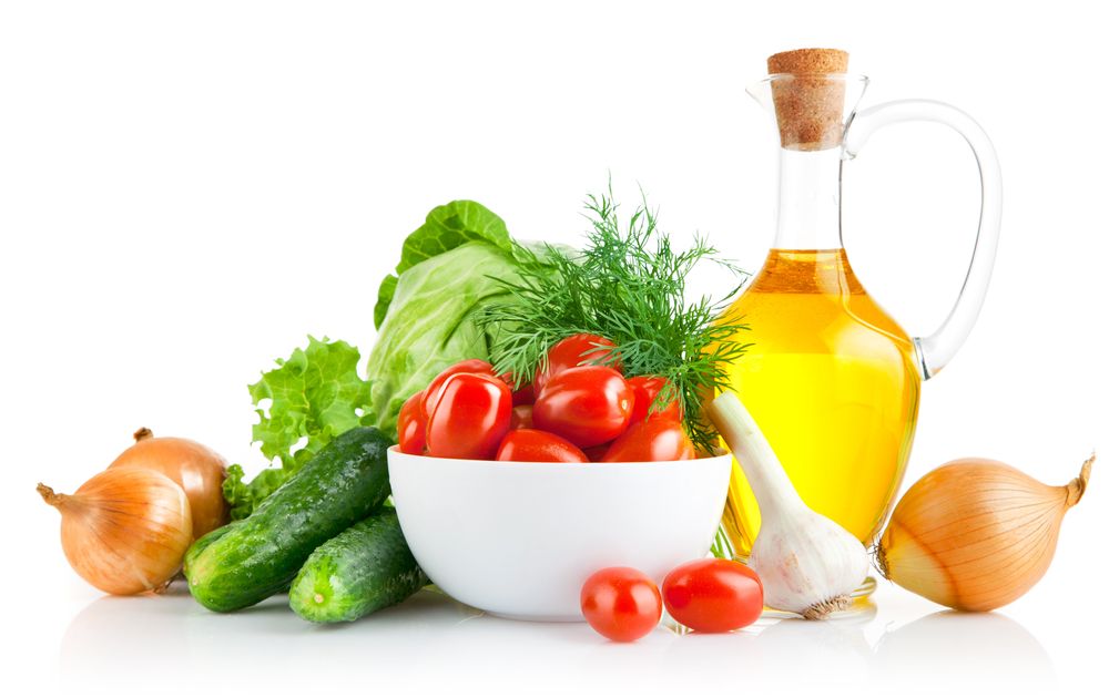 Tomatoes, onions, garlic and other vegetables, along with olive oil sit on a white table. 