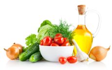 Tomatoes, onions, garlic and other vegetables, along with olive oil sit on a white table. 