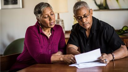 An older couple look at paperwork together while sitting at a table.