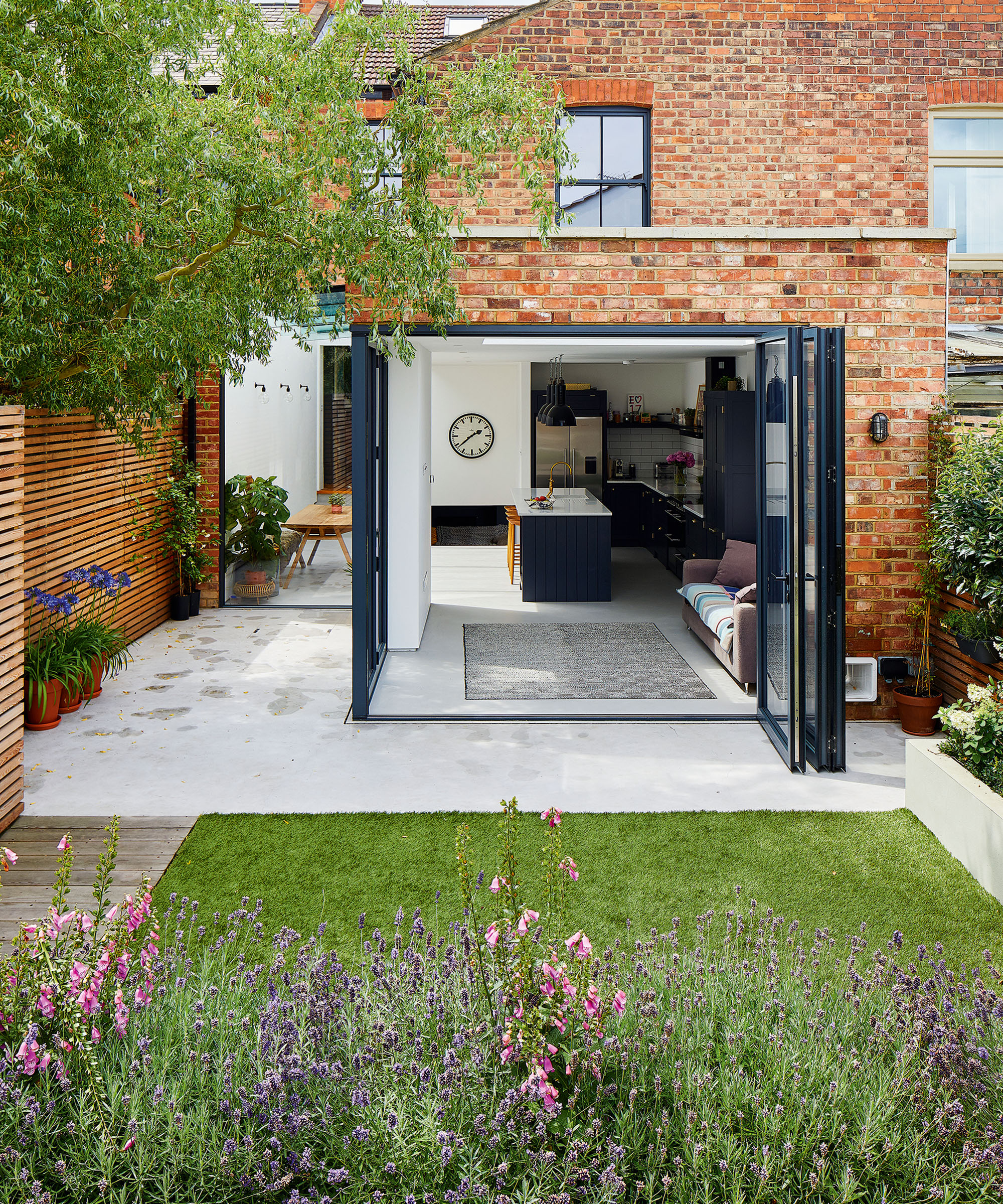 A small garden with a lawn and pale patio next to bifold doors on a kitchen extension