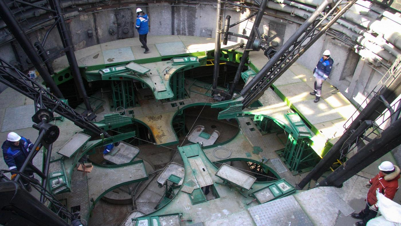 overhead view of a construction site, with three workers wearing blue overalls and a man in red in the scene