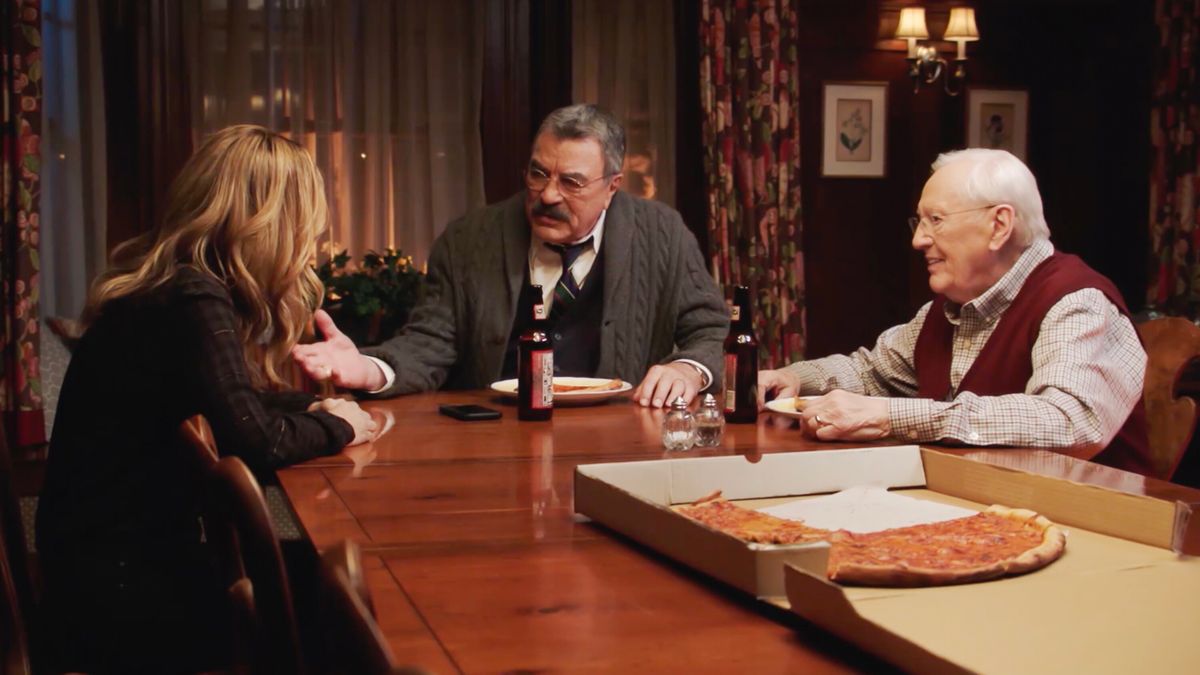 Tom Selleck sits in front of a pizza at the dinner table with Vanessa Ray and Len Cariou in Blue Bloods S14 E9 &quot;Two of a Kind.&quot; 