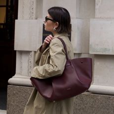 Woman wears trench coat, carries DeMellier New York tote now on sale