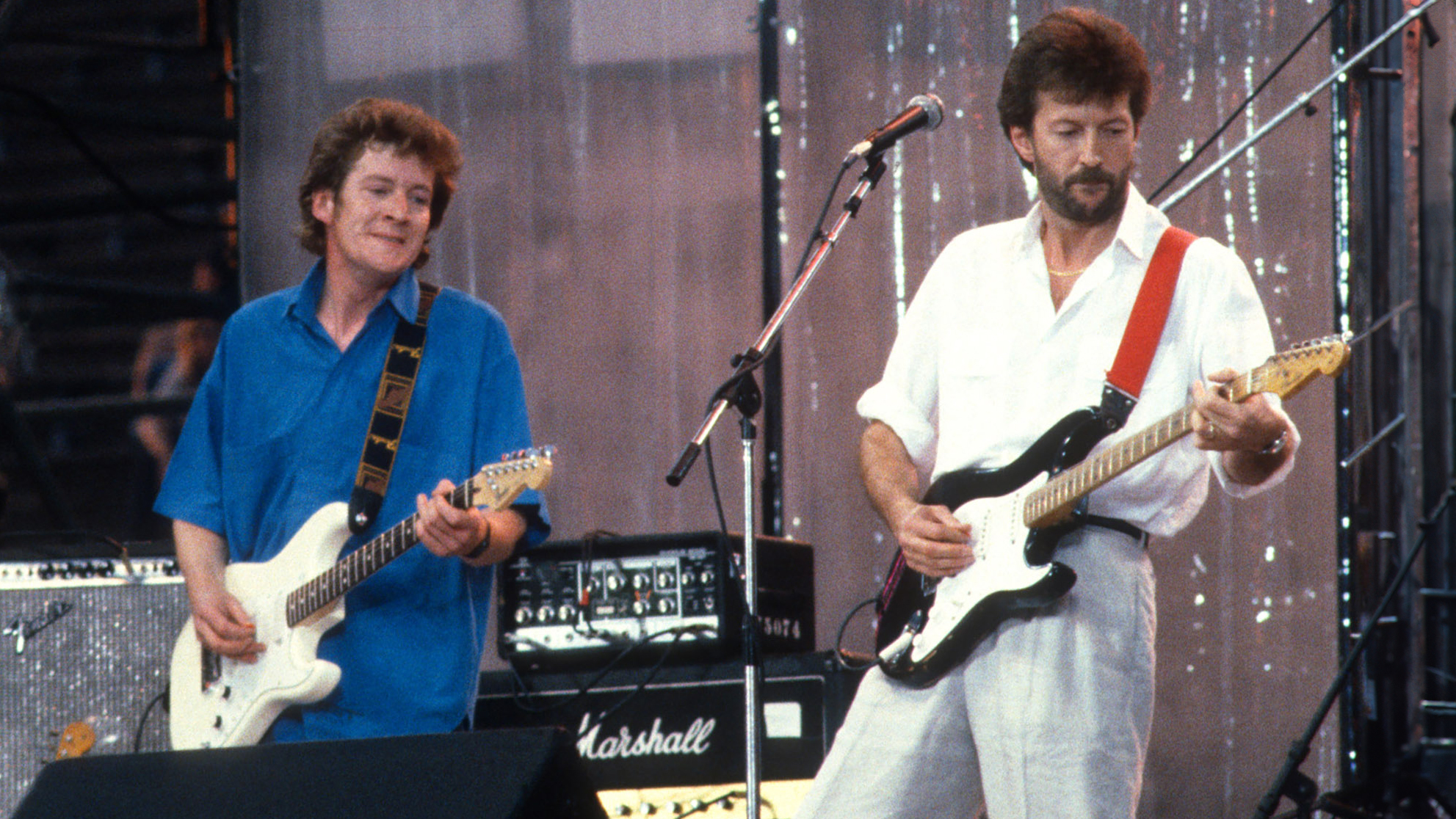 English Rock &amp;amp; Blues musician Eric Clapton (right) performs, with his band, during the Live Aid benefit concert, onstage at JFK Stadium, Philadelphia, Pennsylvania, July 13, 1985. Also visible are Shaun Murphy (left), on tambourine, and Tim Renwick (center), on electric guitar.