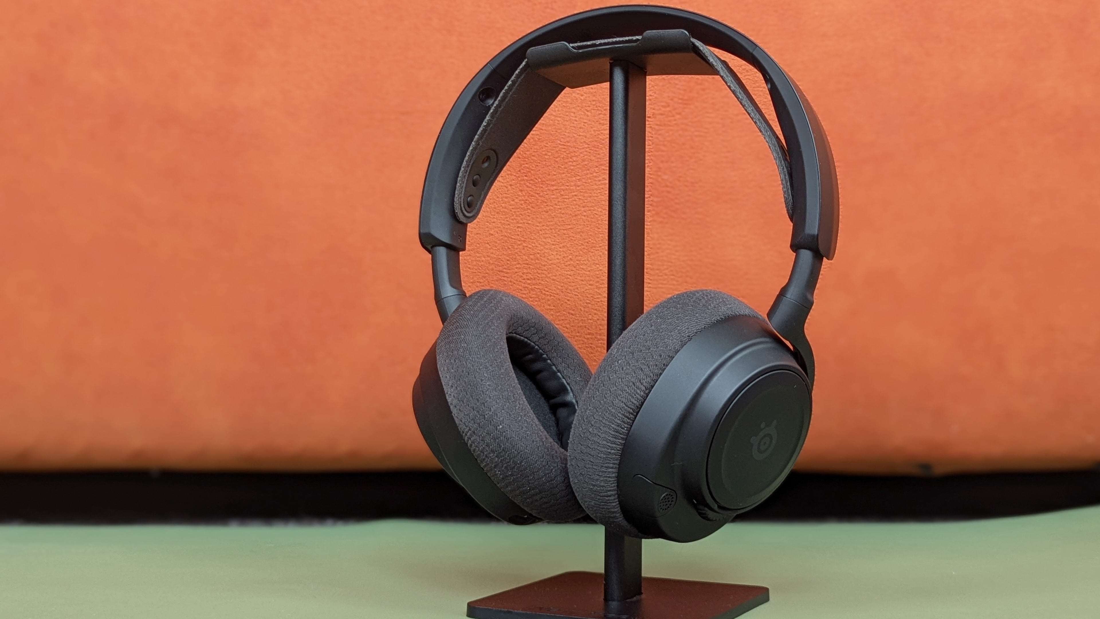 Black headphones resting on a black stand, against an orange and green background