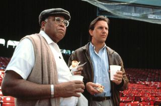 Two men stand in a baseball stadium holding hotdogs