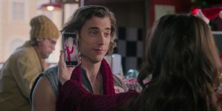 Kath (Lacey Chabert as Kathy Barrett, right) holds up a phone with a picture of a snowman in a scarf, next to a man's (Dustin Milligan as Jack Snowman) face, in 'Hot Frosty.'