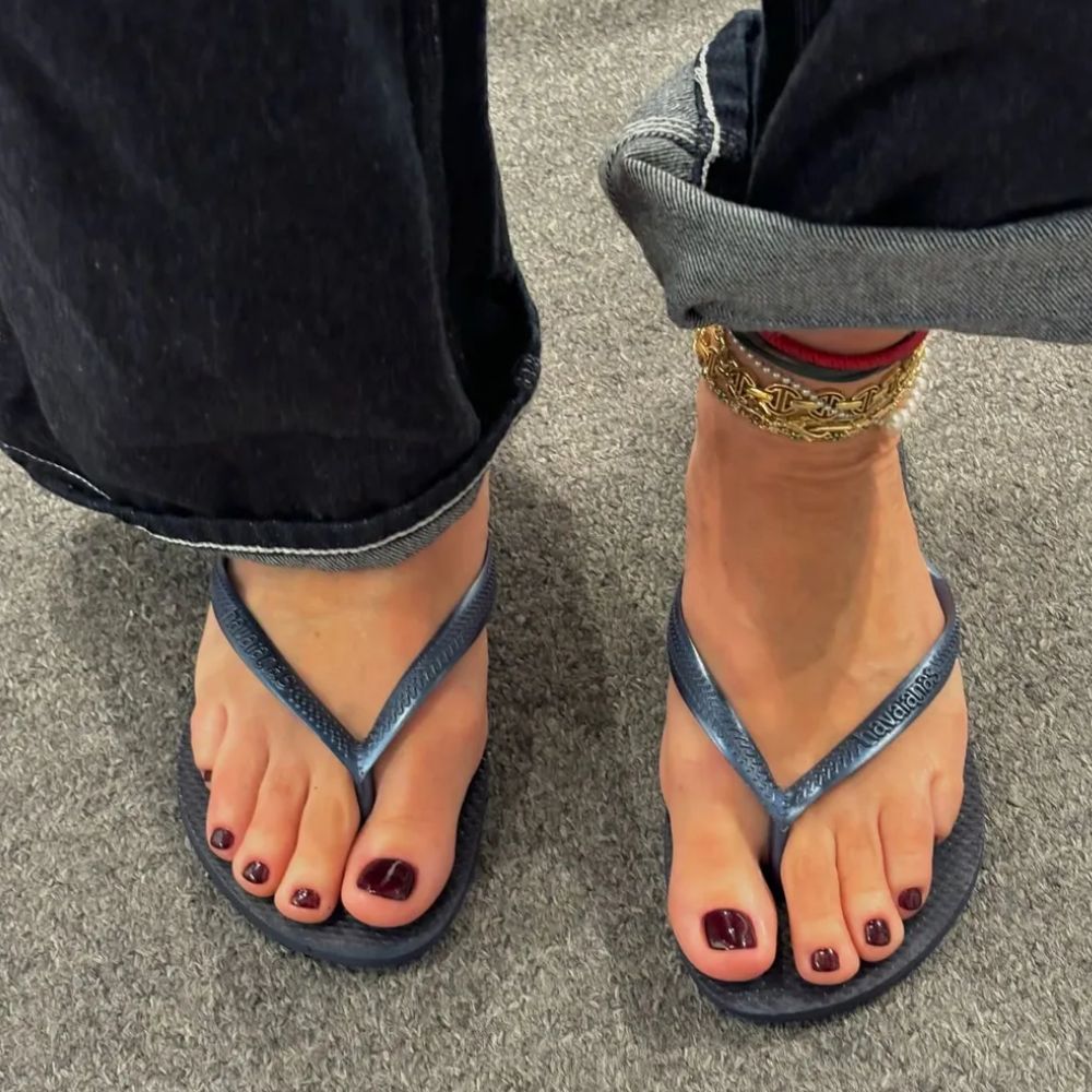 A woman wearing navy flip flops and jeans with a burgundy pedicure