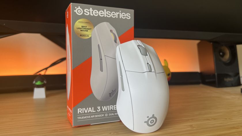 SteelSeries Rival 3 Wireless Gen 2 leaning against packaging with an orange backlight on a wooden desk