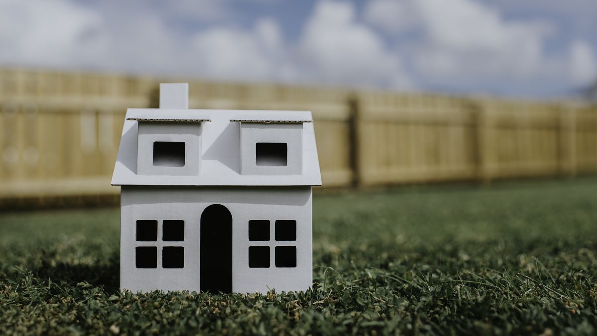 Model of house sitting on grass with fence behind and blue sky