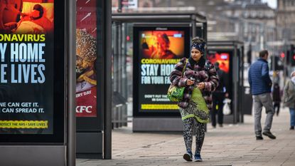 A member of the public walks in front of government lockdown advertisements in Edinburgh