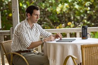 Neville (Ralf Little) sits at a table on his verandah with his laptop closed in front of him. He looks perturbed.